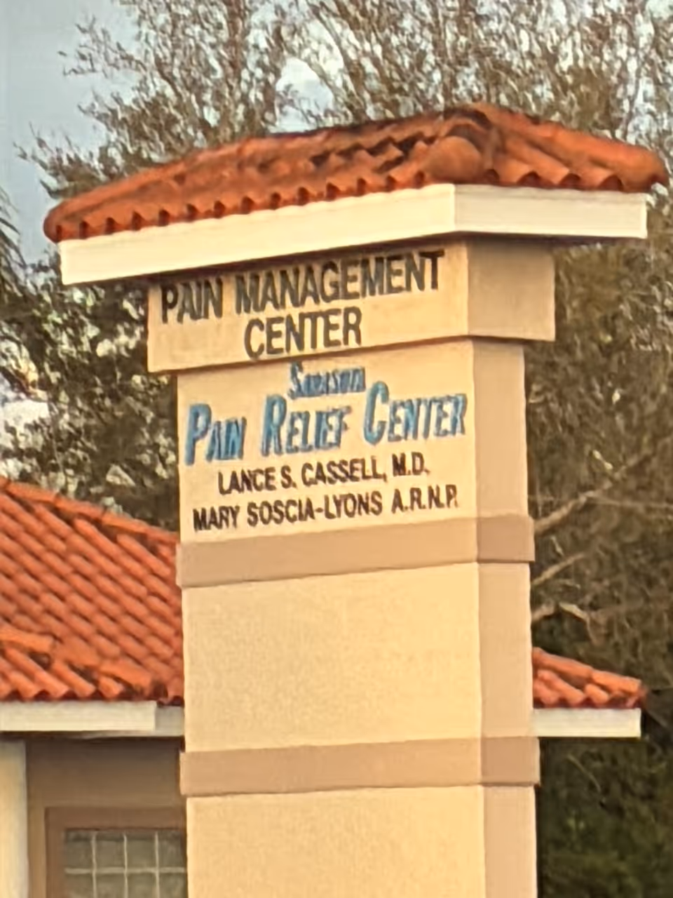 Exterior sign pillar reading Pain Management Center and Pain Relief Center with terracotta roof.