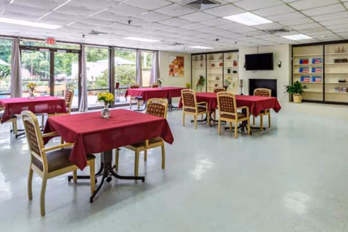 Senior living dining area with red tablecloths, chairs, shelves, and large windows.