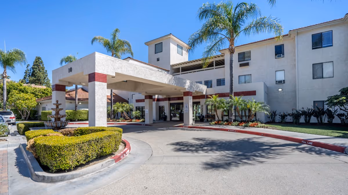 Exterior view of Brookdale Irvine with a porte-cochère entrance, palm trees, and manicured landscaping.