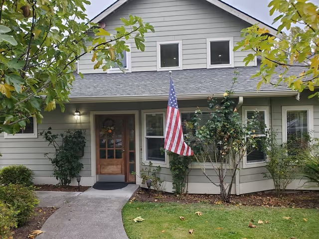 Front exterior of a light-green house with an American flag and landscaped yard.