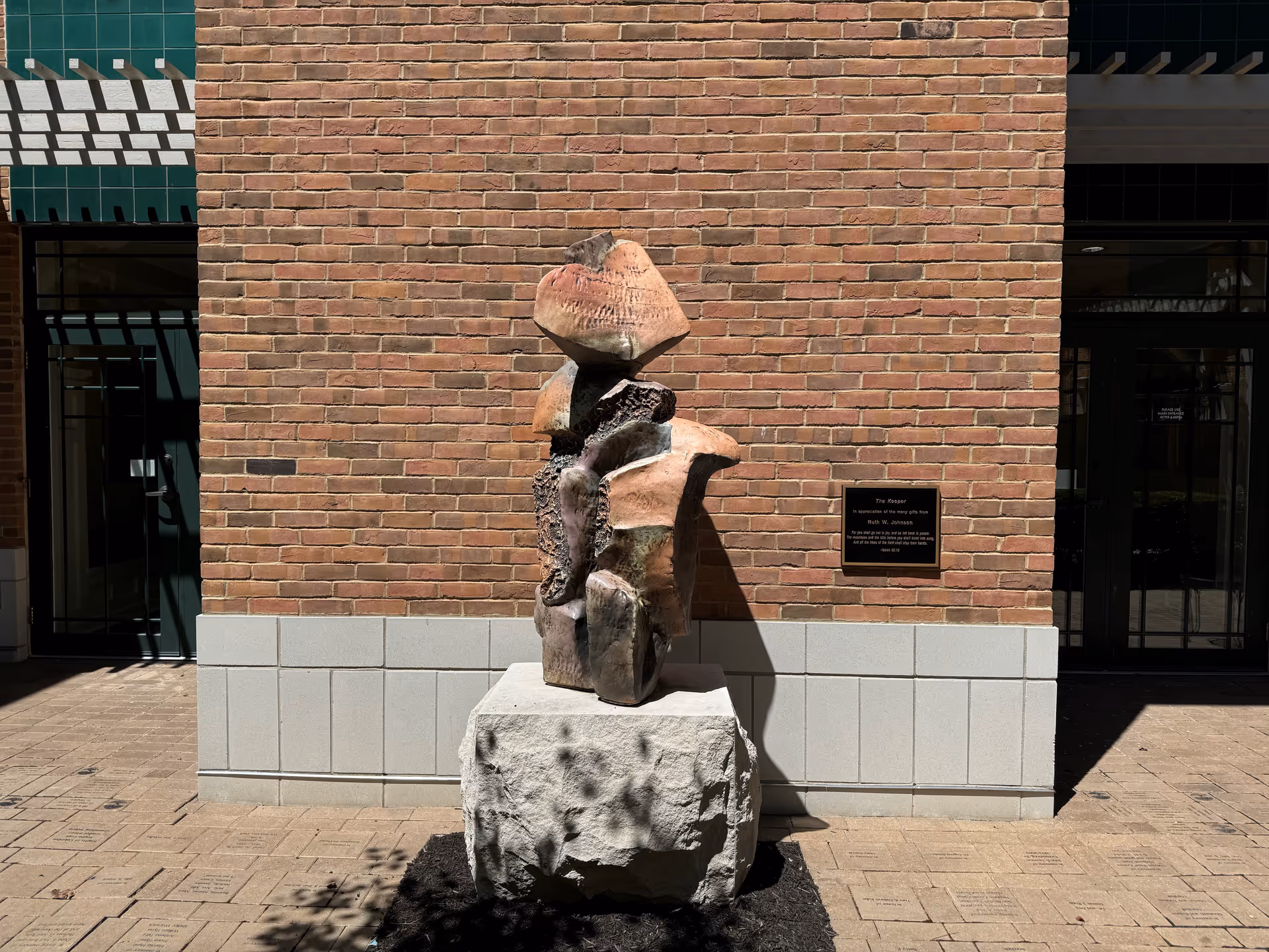 Stone sculpture on pedestal in front of a brick building entrance with plaque.