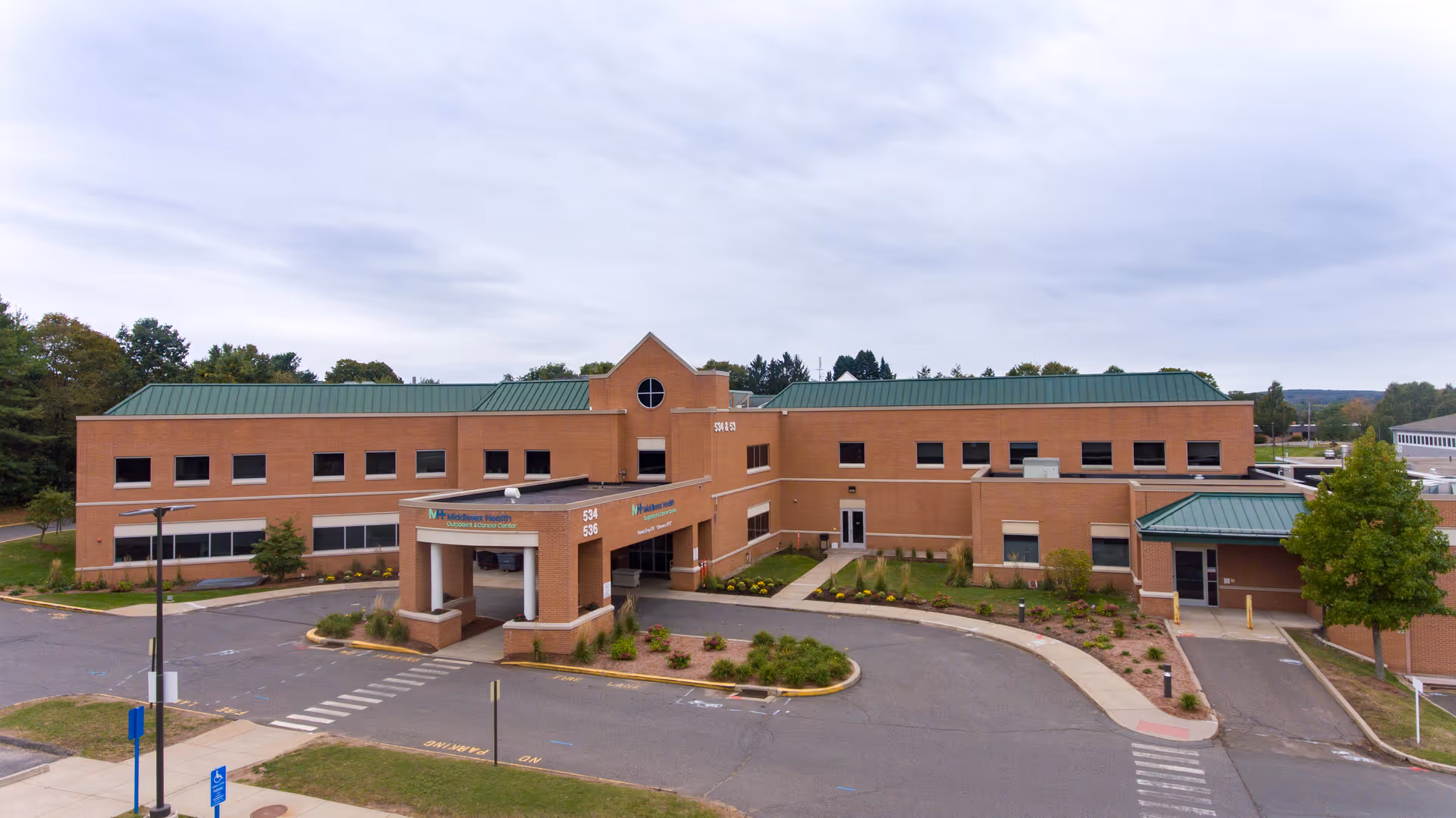 Brick building with green roof and covered entrance, parking lot in front.