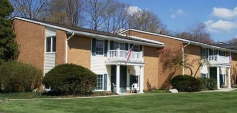 Brick senior living building with white balconies and a manicured lawn.