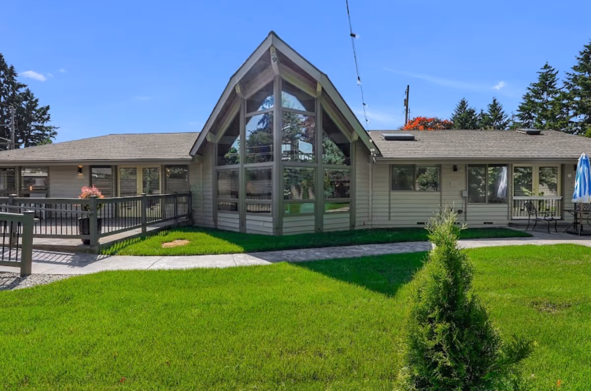 Single-story facility with glass-front entrance, green lawn, outdoor seating, and a fenced walkway.