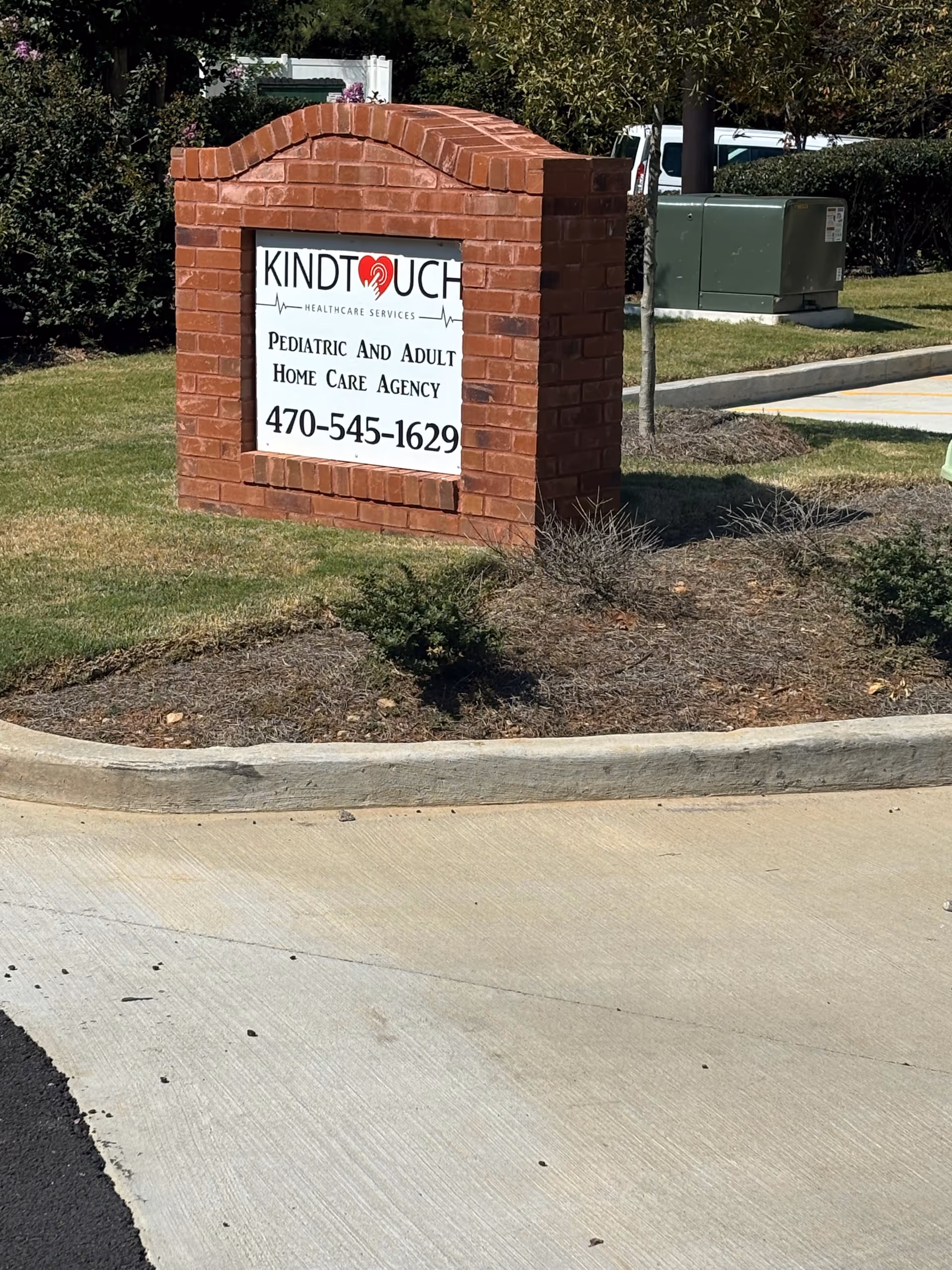 Brick sign for KindTouch Healthcare Services outside entrance with landscaping.