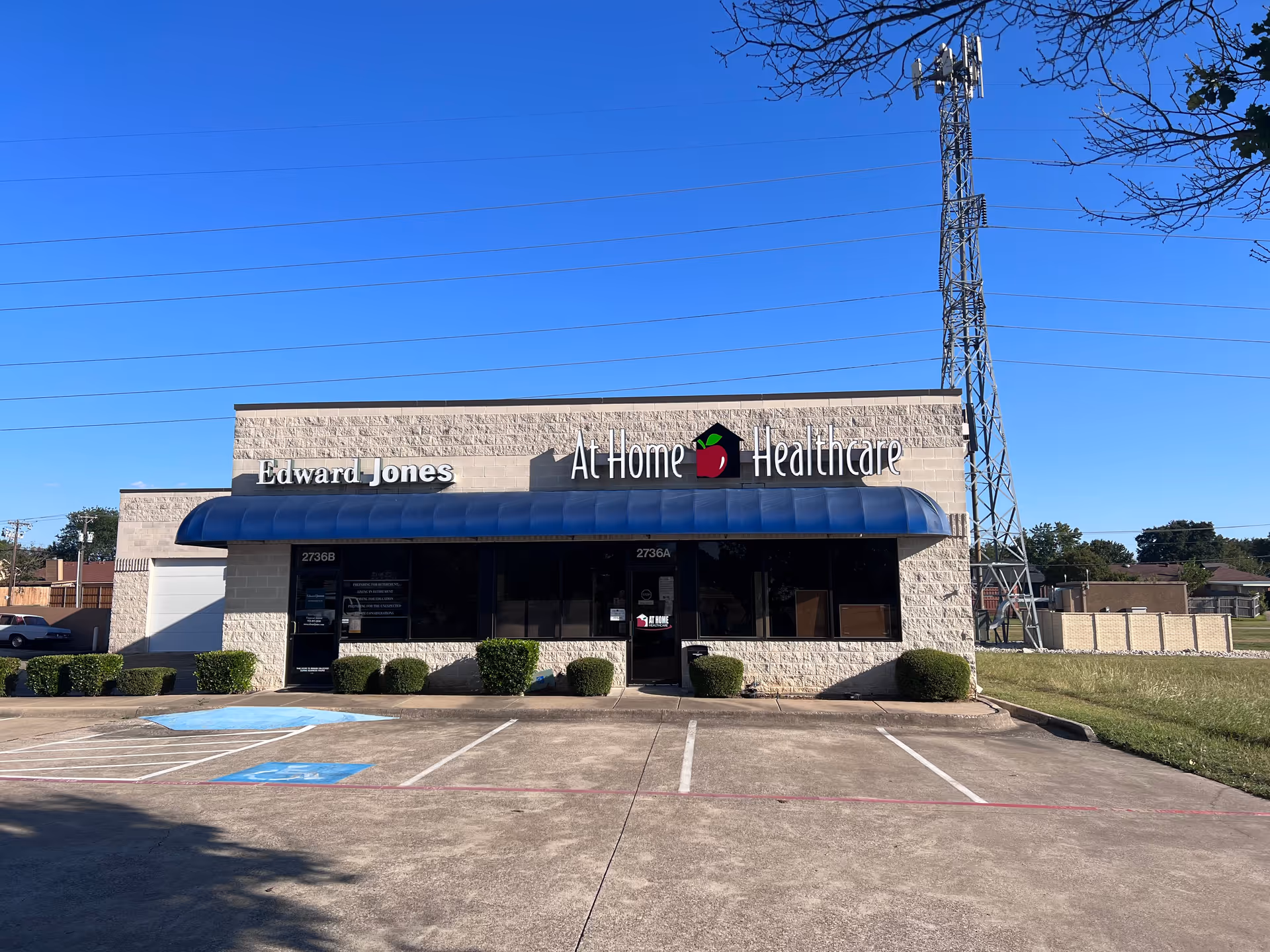 Exterior view of a single-story building with a blue awning and parking lot.