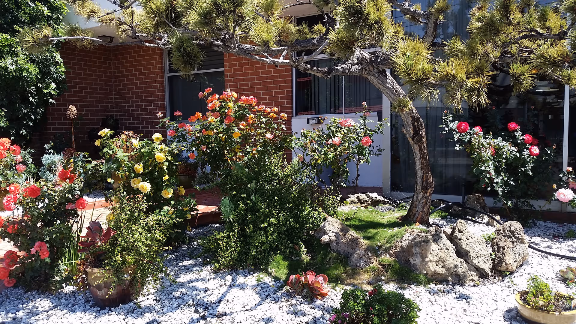 Front exterior of a brick senior facility with a flowering garden and rocks.
