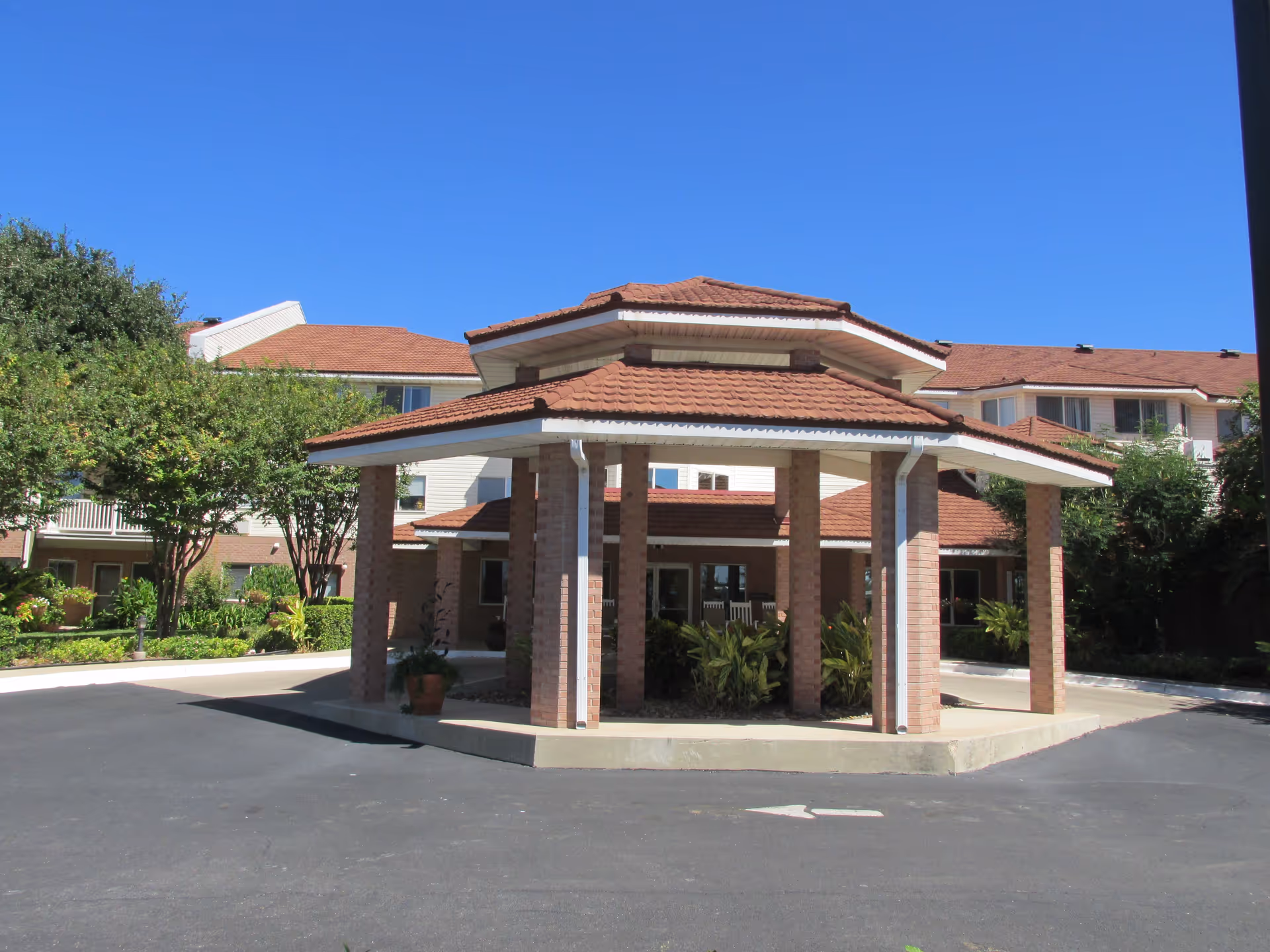 Brick-faced senior living facility entrance with a covered porte-cochere and clear blue sky.