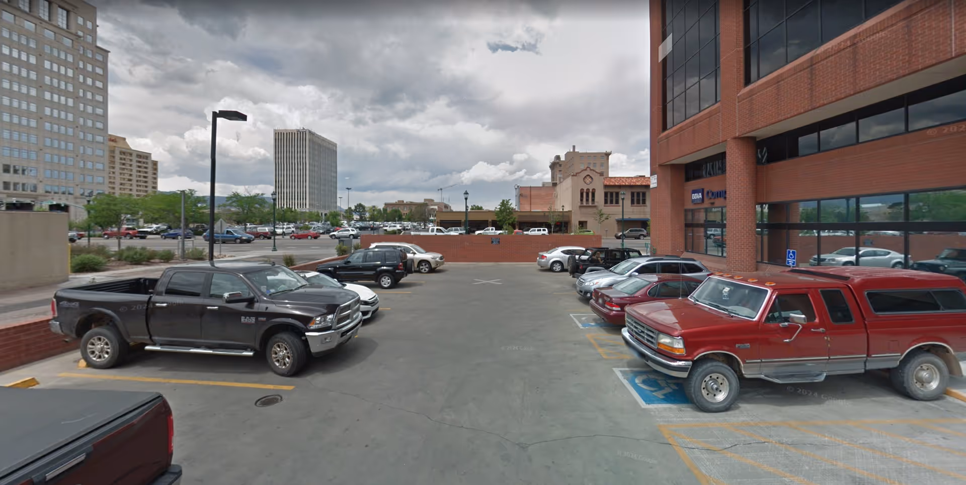Parking lot in front of a brick building with several parked cars and a cloudy sky.