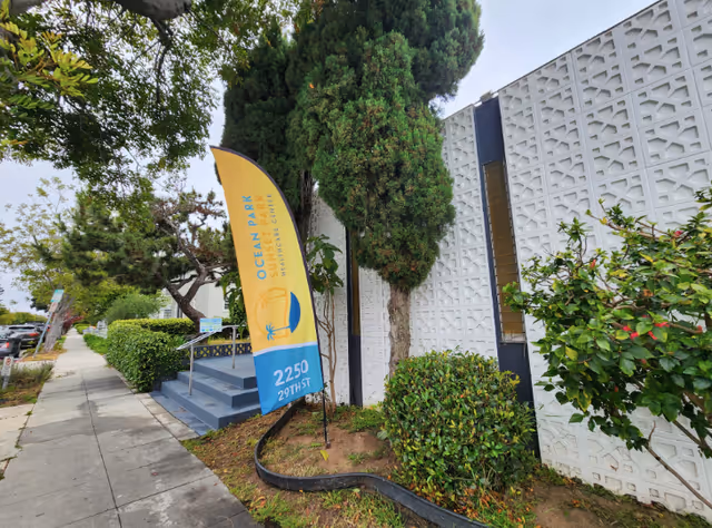 Exterior view of a facility with a patterned white wall and a yellow banner beside steps.