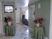 Hallway in a senior living facility with green walls, round tables, and pink flowers.