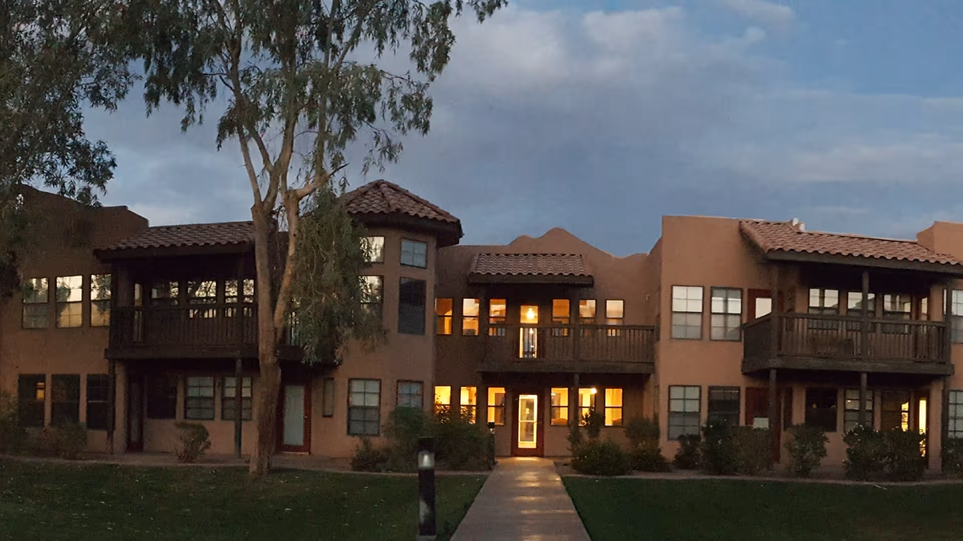Exterior of Emerald Springs Senior Living, two-story tan stucco building with balconies and lit entrance.