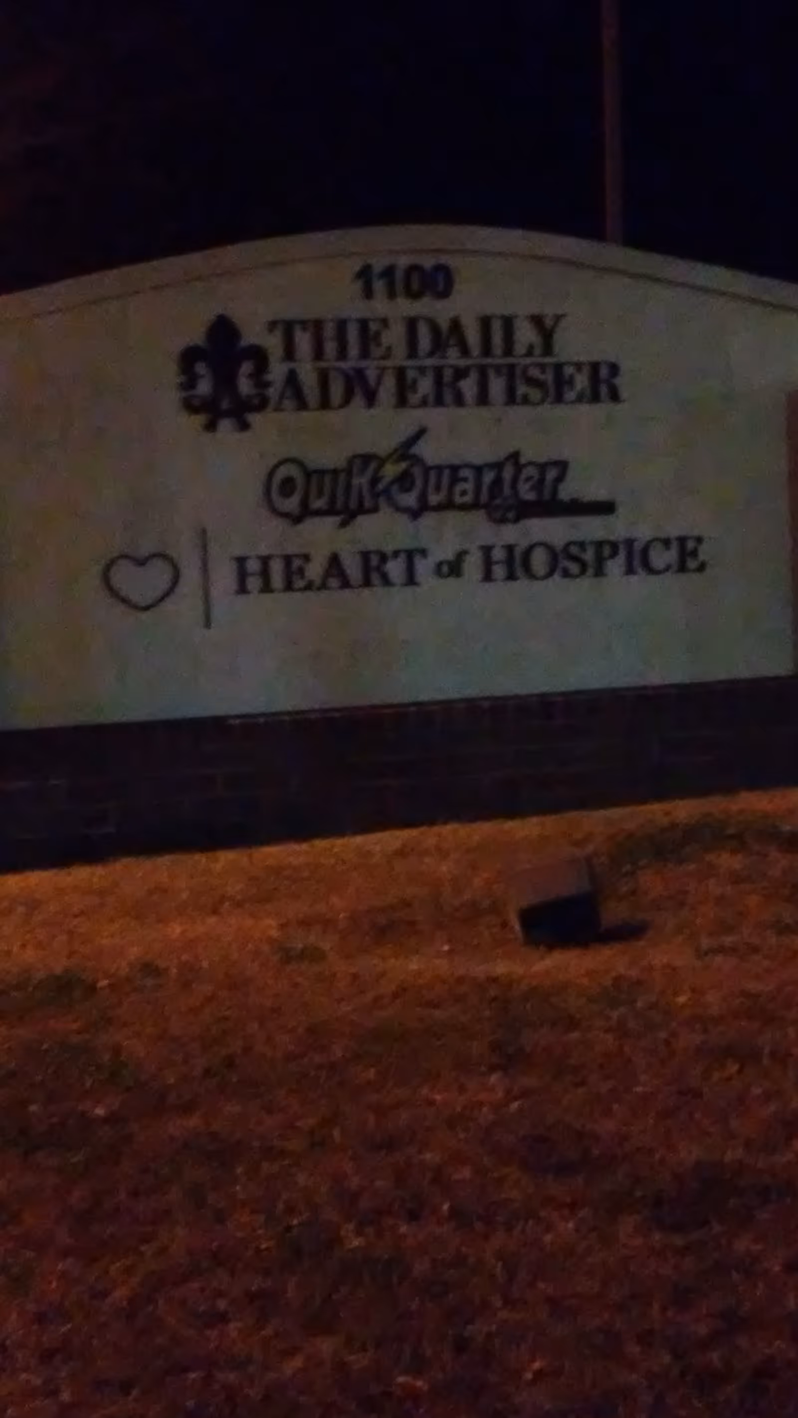 Nighttime exterior sign reads Heart of Hospice beside The Daily Advertiser.