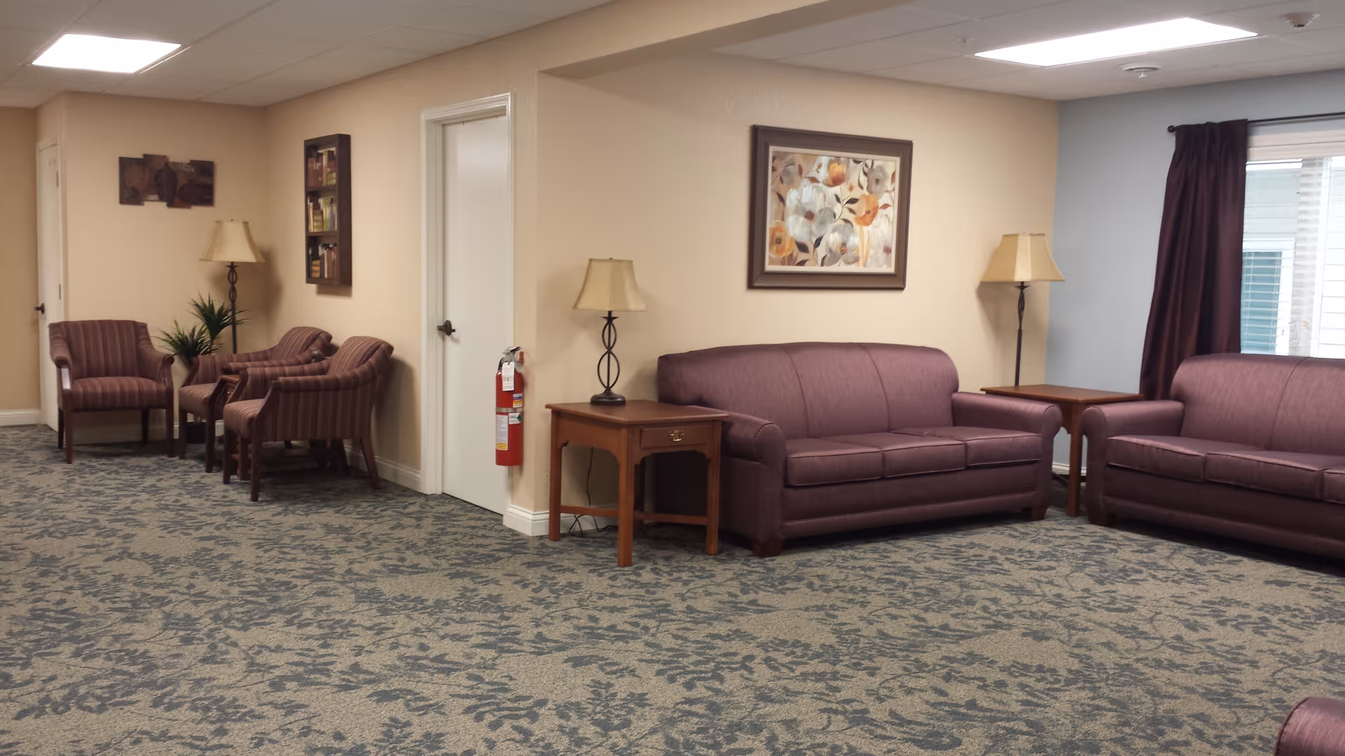 Interior senior living lounge with purple sofas, chairs, lamps, and artwork.