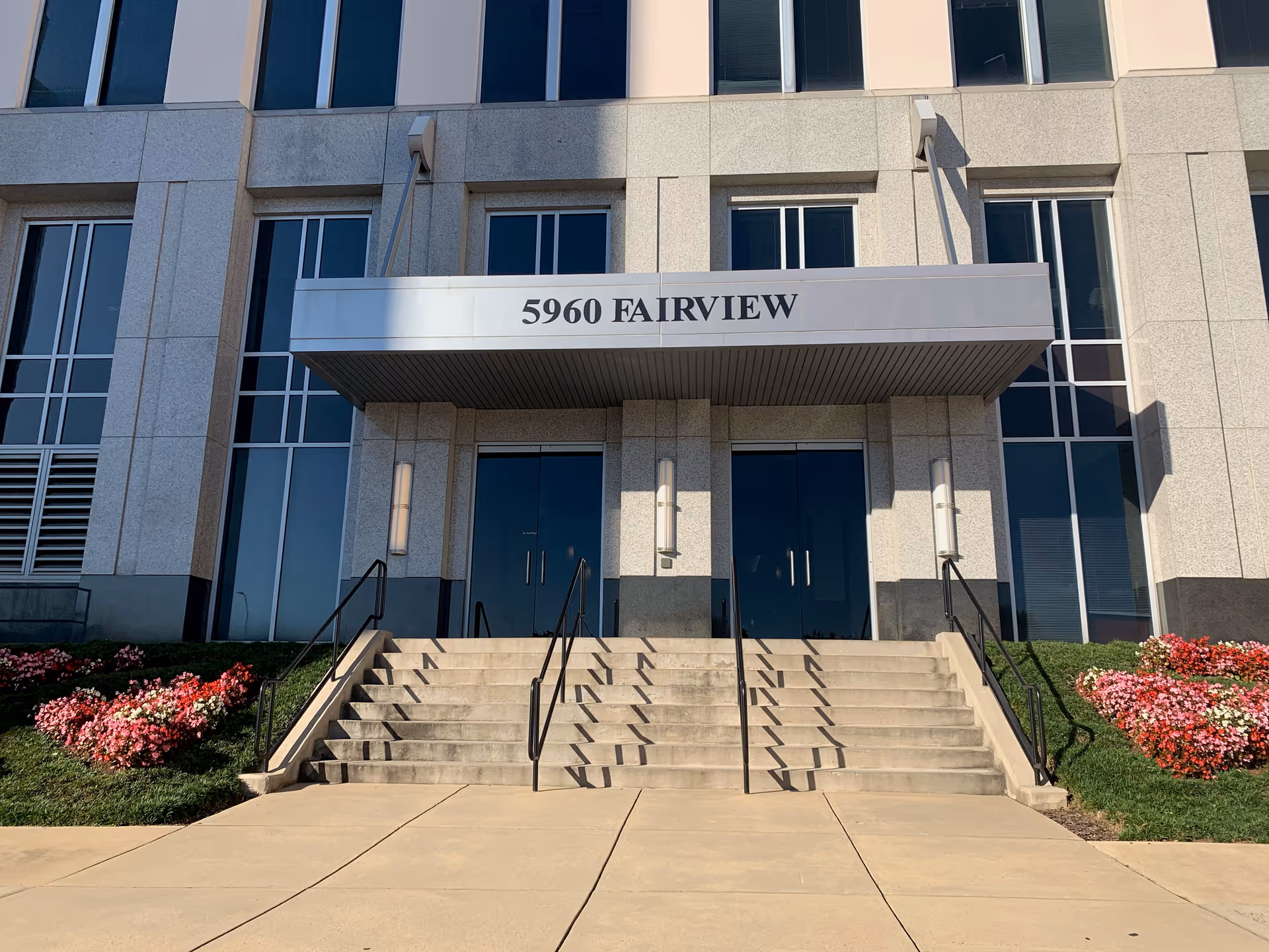 Modern building entrance with stairs, sign reading 5960 FAIRVIEW, and flower beds on both sides.