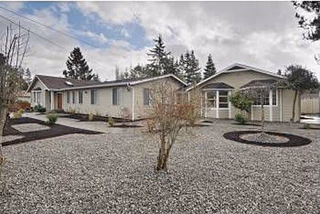 Single-story beige residential building with gravel landscaping and circular planting beds under a cloudy sky.