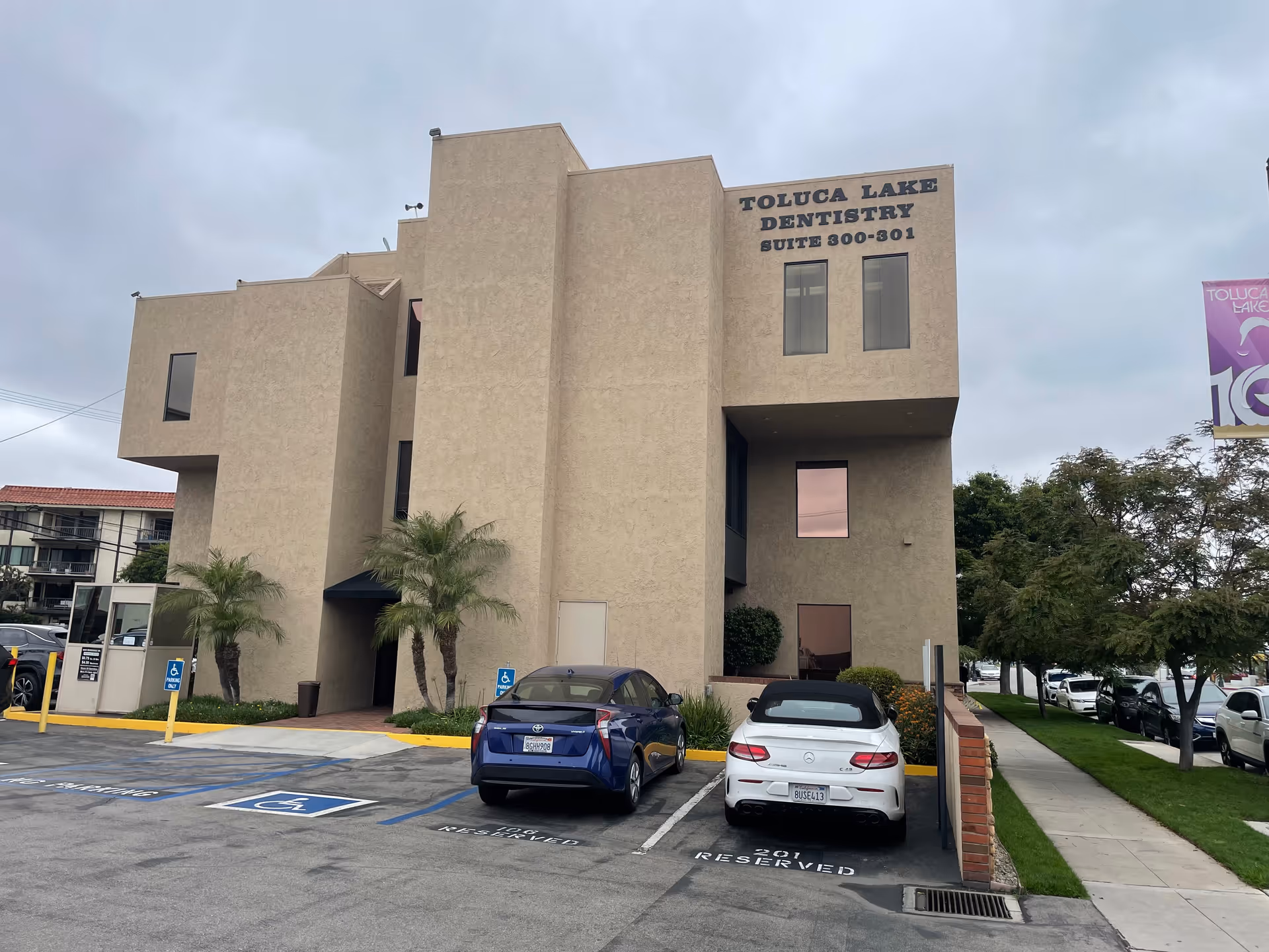 Tan modern building with Toluca Lake Dentistry sign, adjacent parking lot, and palm trees.