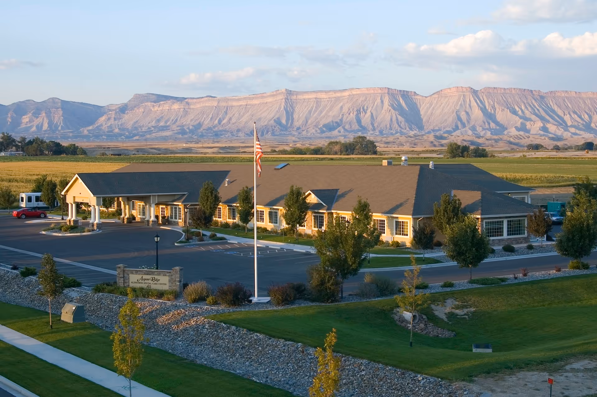 Exterior view of Aspen Ridge Alzheimer's Special Care Center with parking, flagpole, and mountain backdrop.