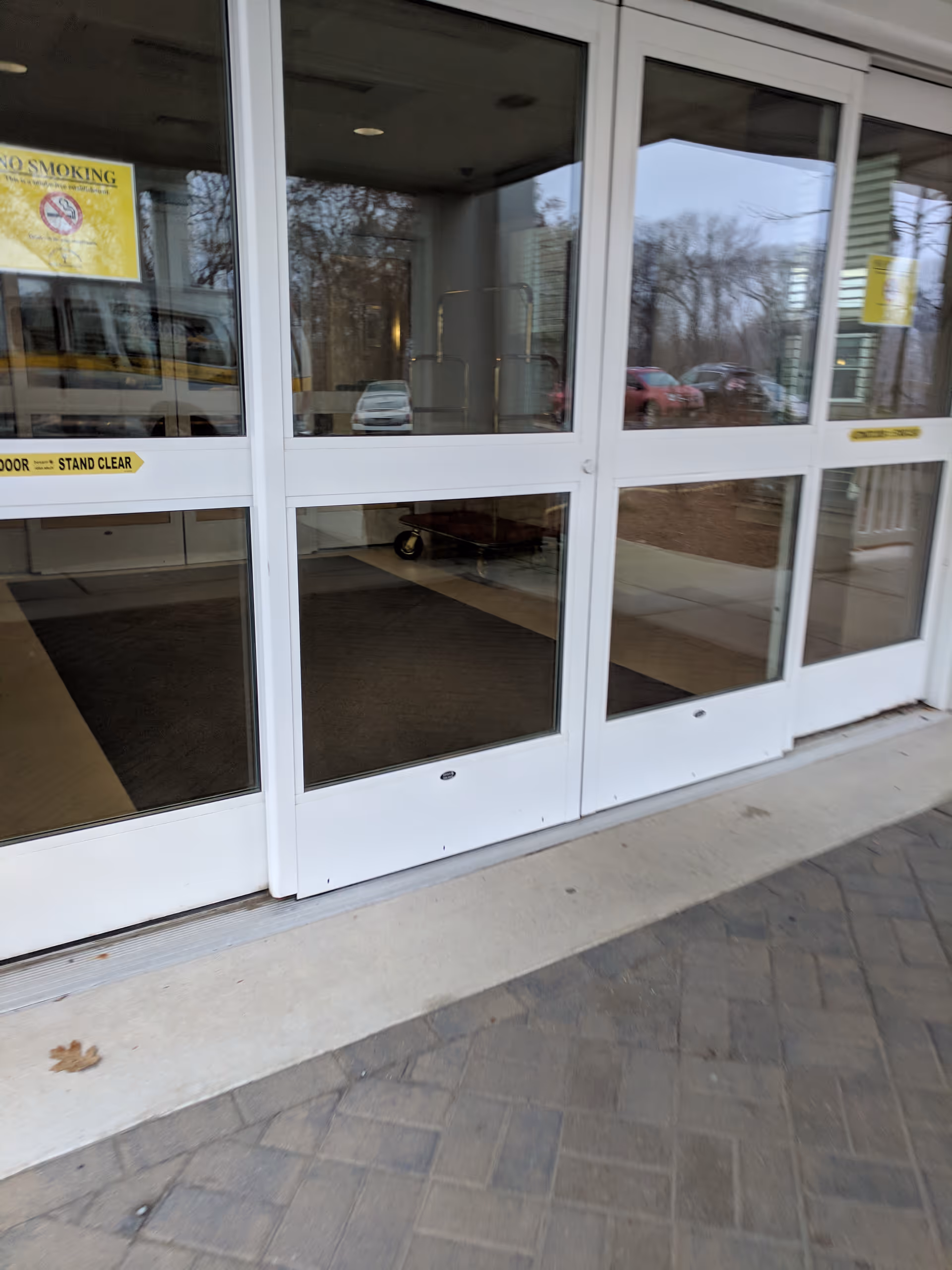 Glass entrance doors of a senior living facility with signage and a sidewalk.