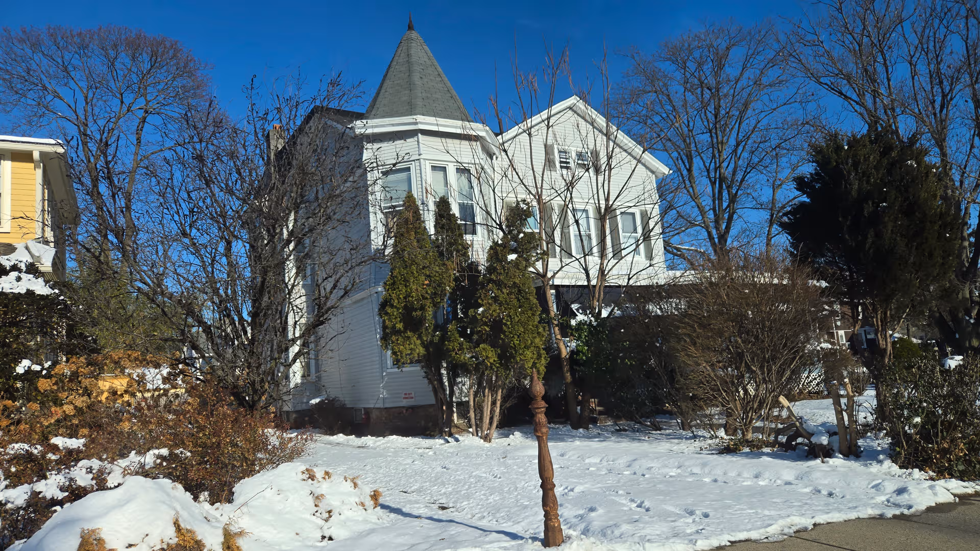 White turreted senior living building with snow, bare trees, and blue sky.