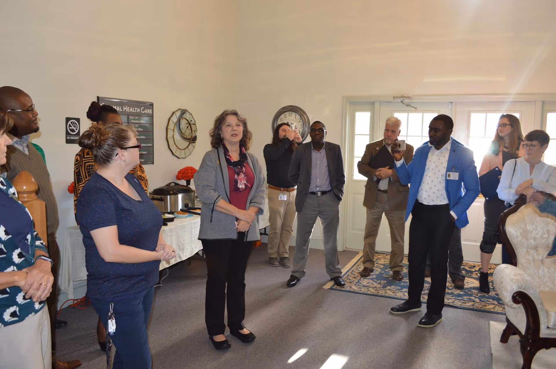 Group of adults in a lobby-like interior, with some taking photos, at Optimal Health Care Inc.
