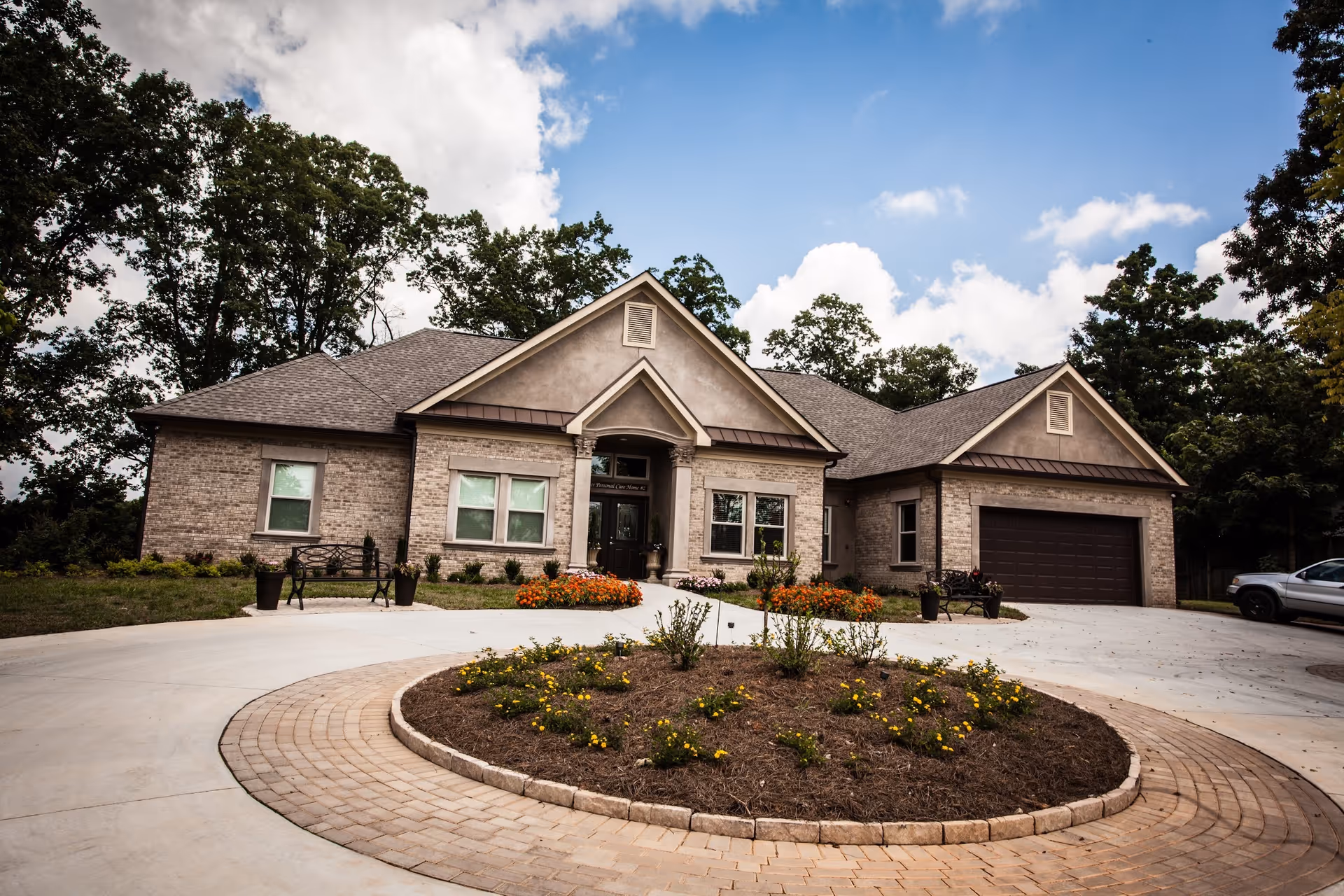 Brick senior living facility with circular driveway, landscaped flower beds, and a two-car garage entrance.