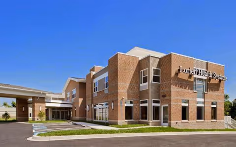 Front exterior of a two-story brick building labeled "Lorien Health Systems" with a porte-cochère entrance under a clear blue sky.
