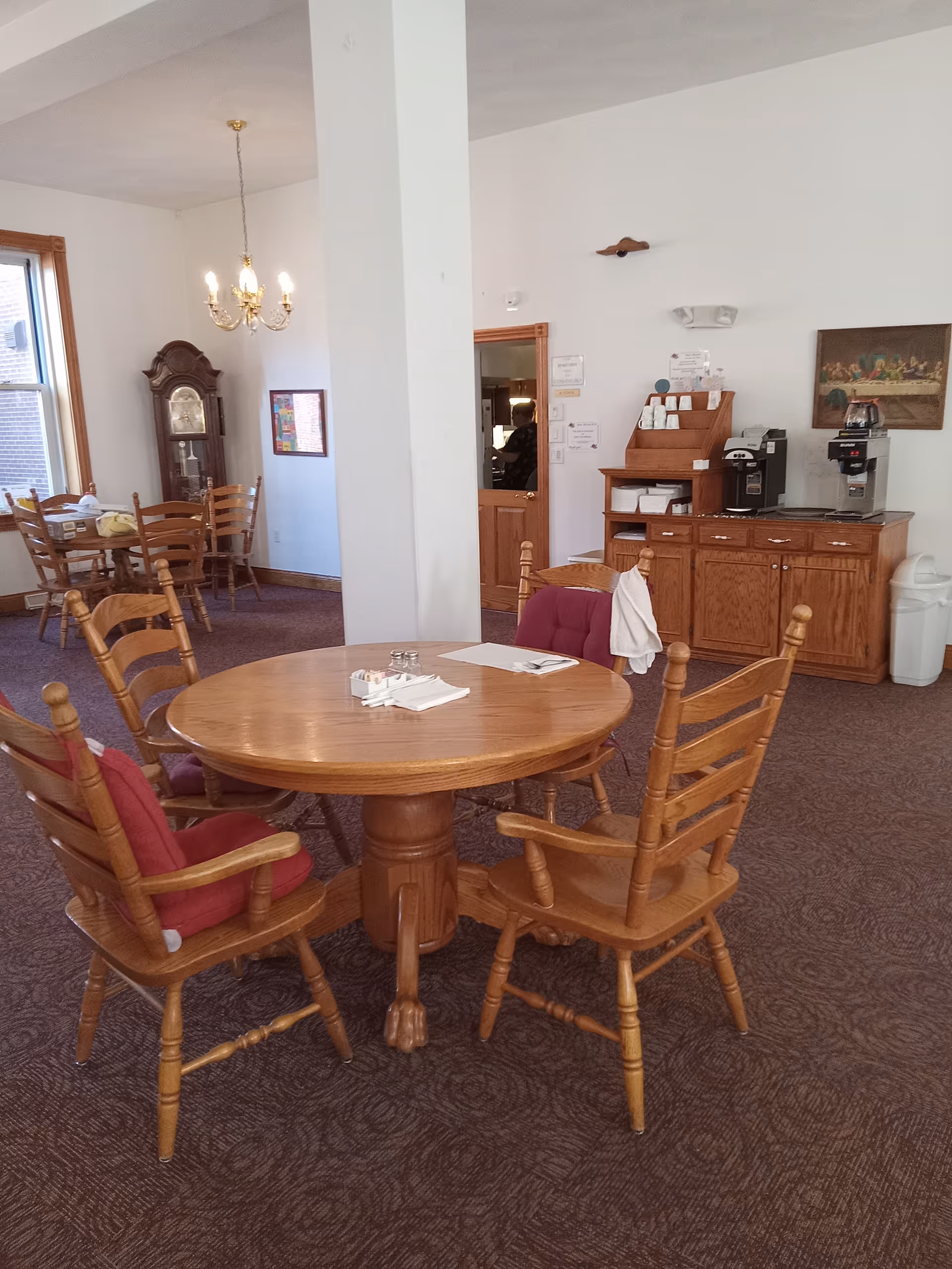 Round wooden dining table with chairs in a shared senior living dining room.