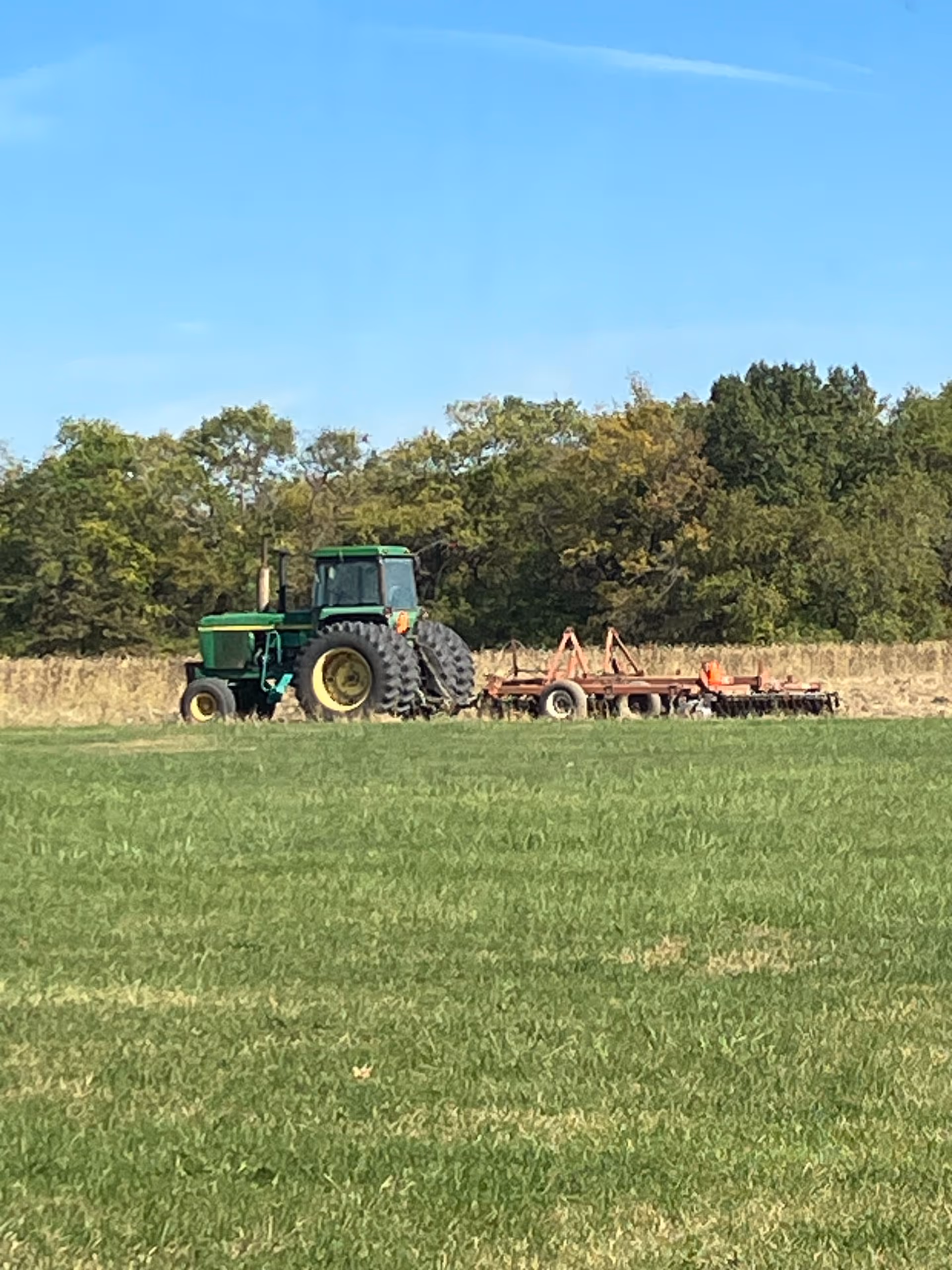 Green tractor with attached implement sits idle in a grassy rural field.