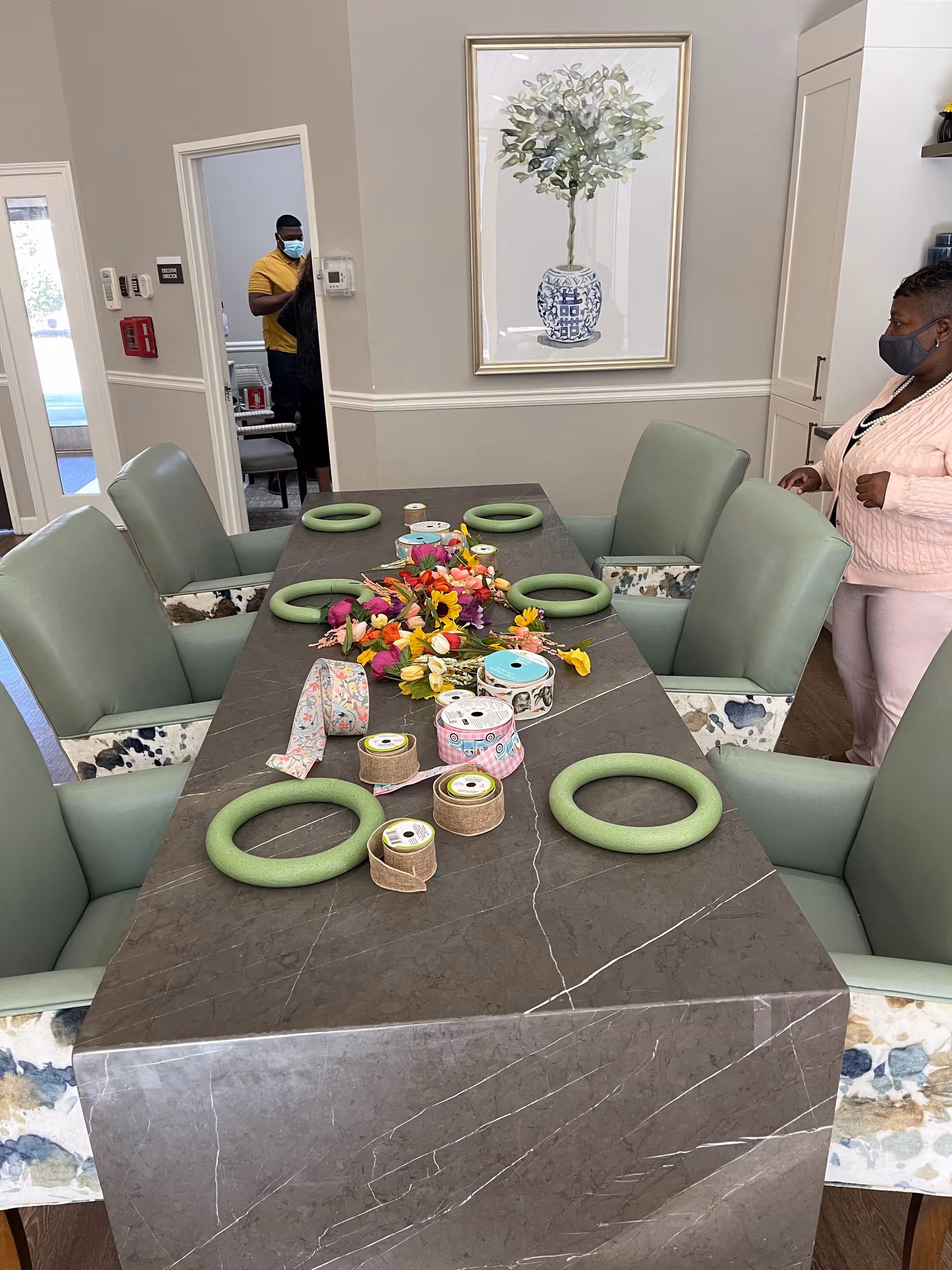 A long dining table with teal chairs and craft supplies in a senior living dining area.