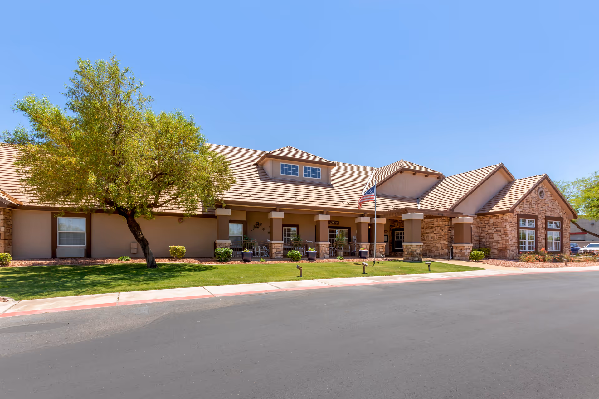 Single story senior living facility with brick facade, green lawn, and flag near entrance.