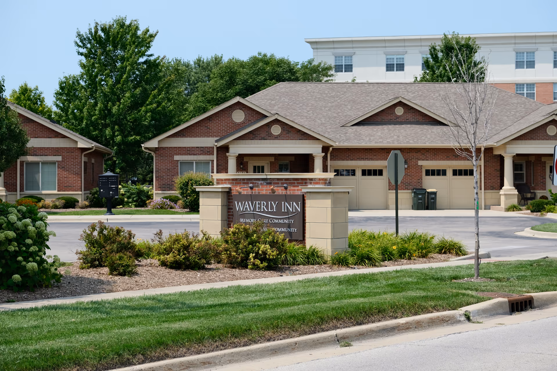 Front entrance sign reading 'Waverly Inn Memory Care Community' with landscaped grounds and brick facility buildings behind it.