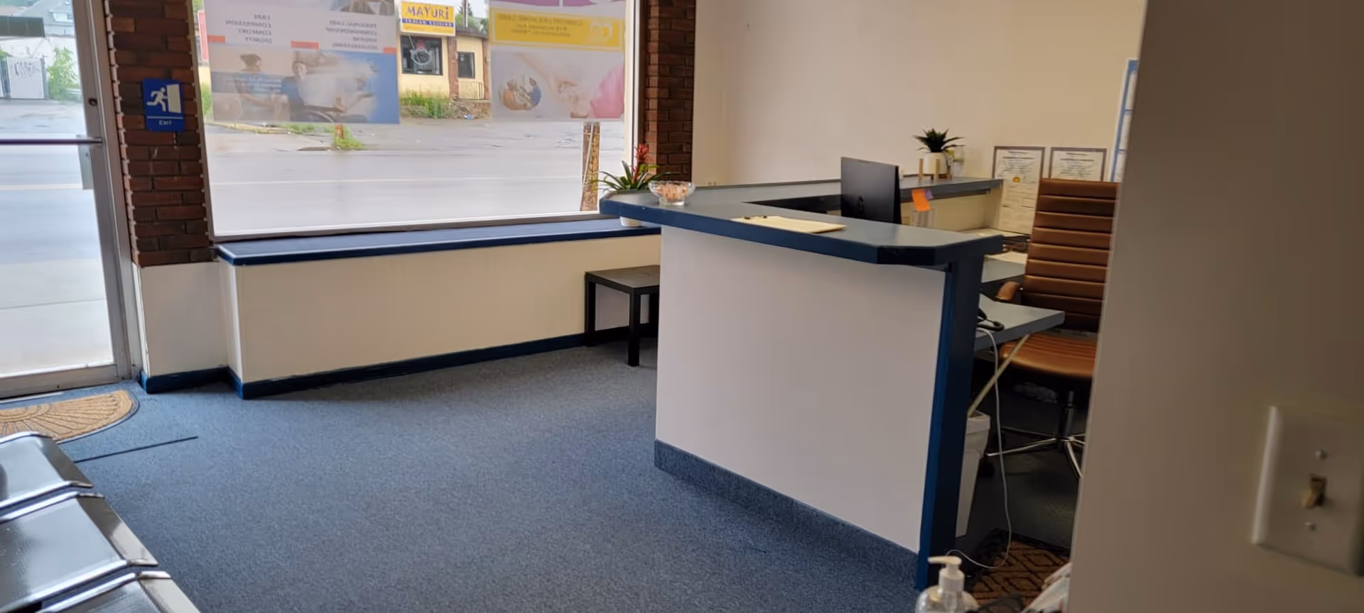 Reception desk in a bright lobby with a computer, windows, and seating area.