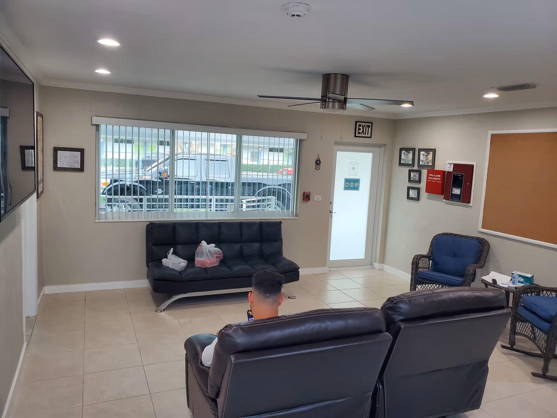 A waiting area with black leather sofas, blue chairs, and a window view.