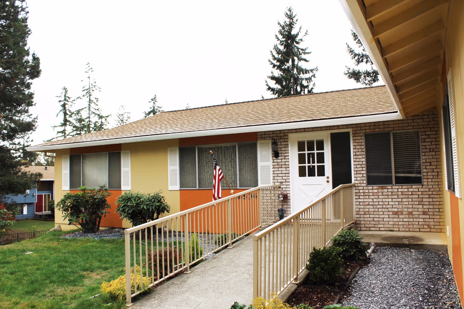 Single-story building exterior with ramp, railing, windows, and an American flag by the entrance.