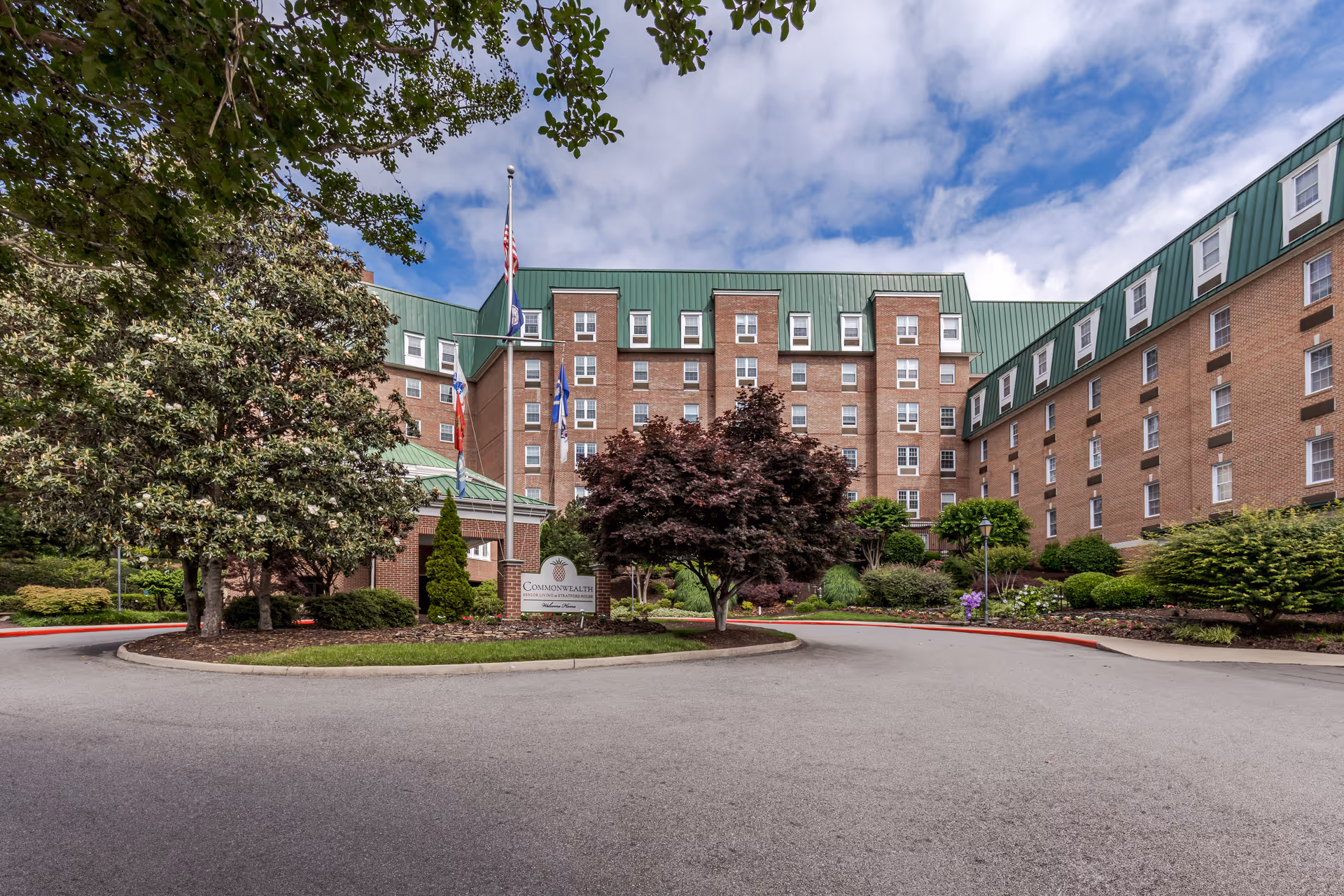 Brick senior living building with green roof, flags, and circular driveway.