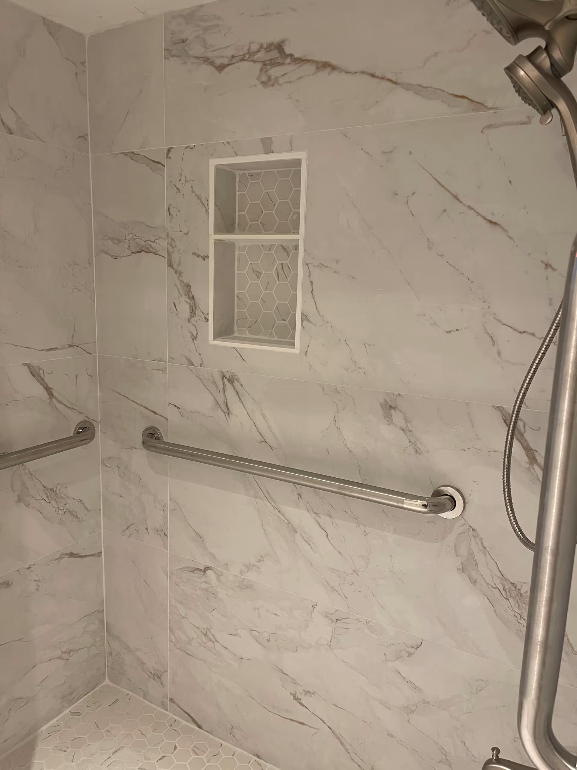 Marble-tiled bathroom shower with grab bars and a small recessed niche.