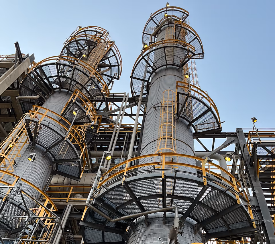 Two cylindrical industrial towers with orange railings and spiraling staircases reach skyward.