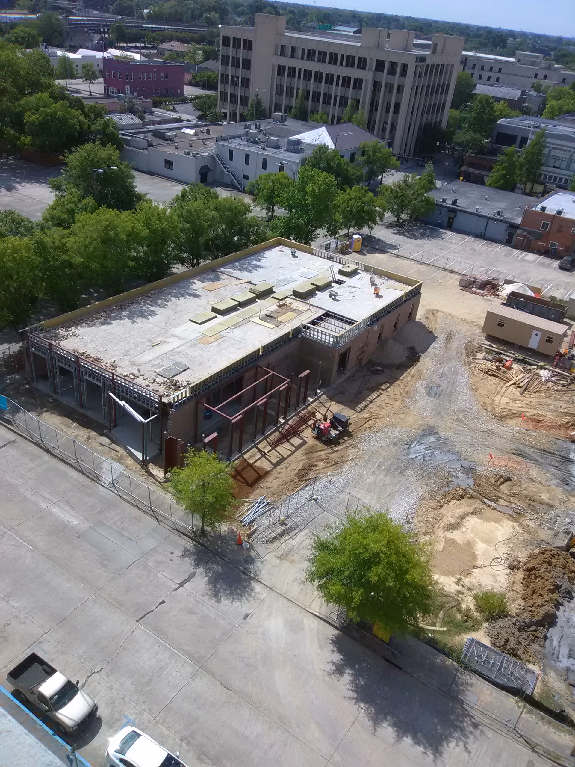 A construction site next to a partially built low-rise building with surrounding trees.
