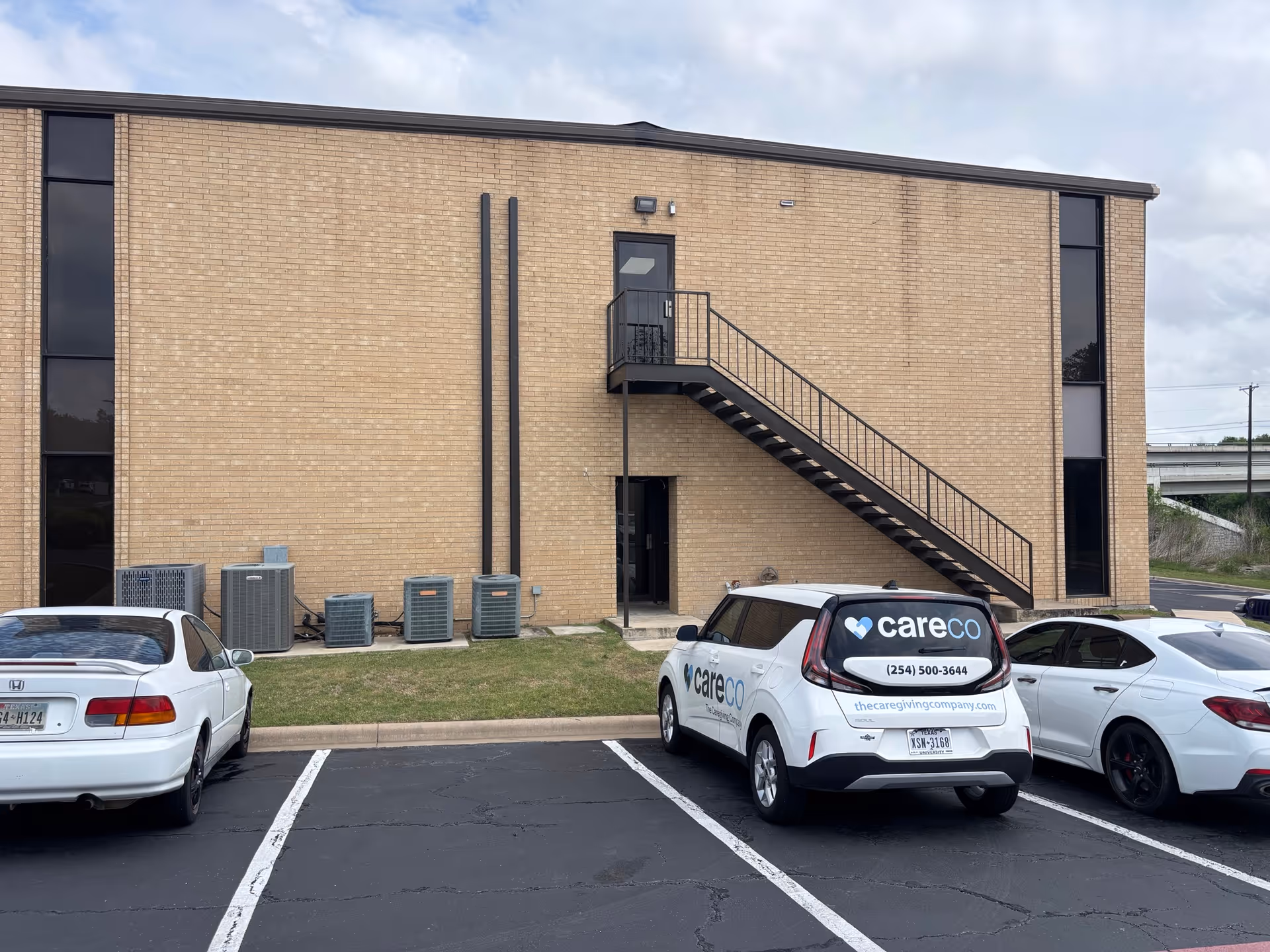 Brick building exterior with a metal staircase, parking lot, and a careCo van.