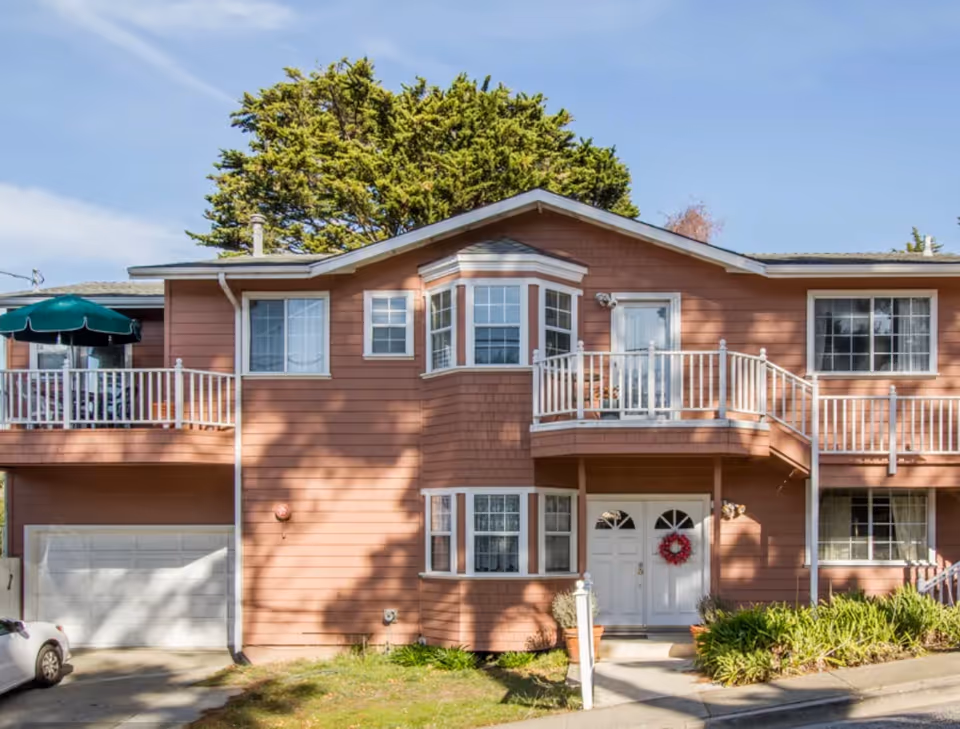 Two-story peach-colored senior living building with white railings, balconies, and a front entrance.
