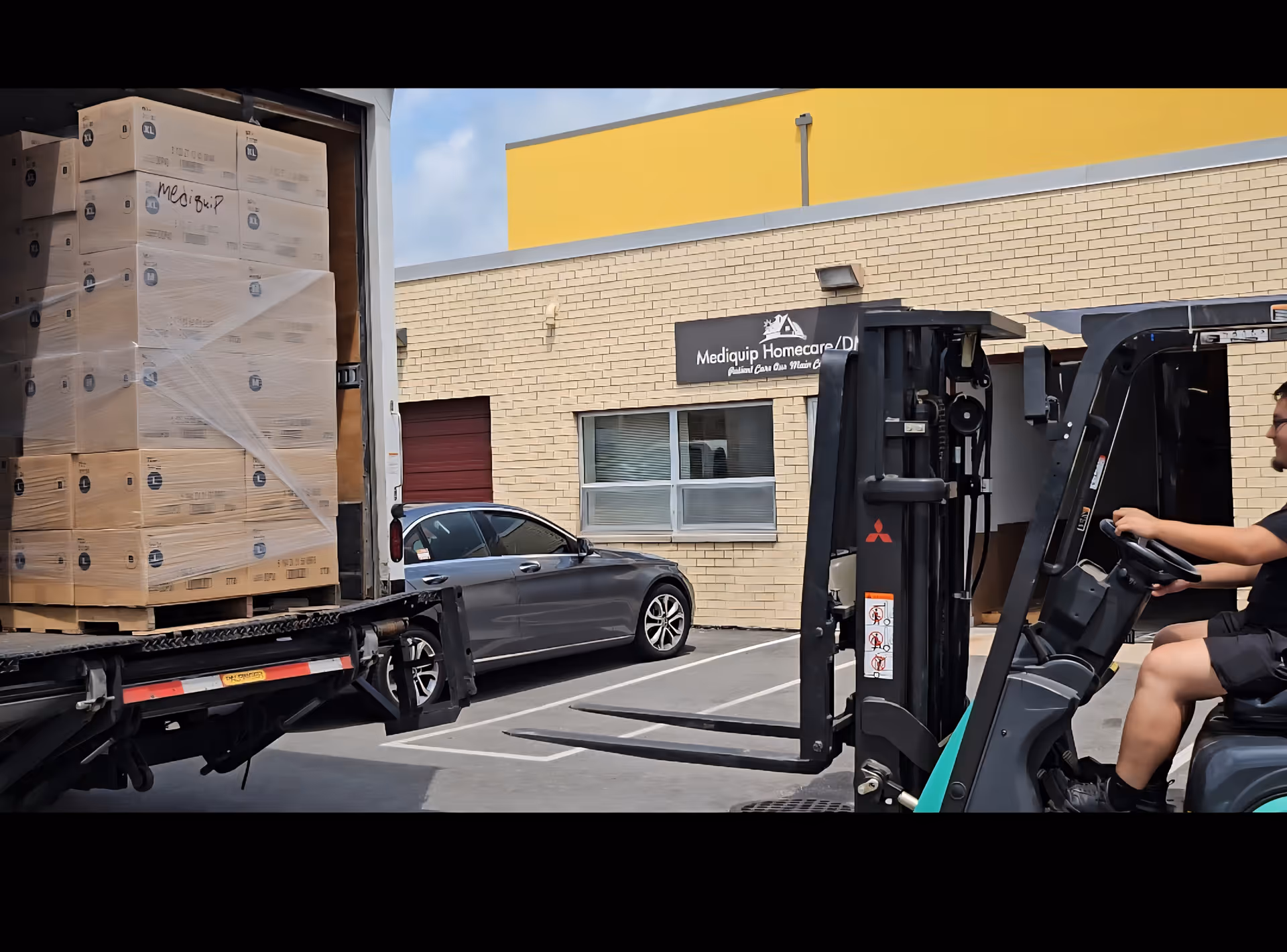 Forklift operator loads boxed supplies from a truck at a Mediquip facility exterior.