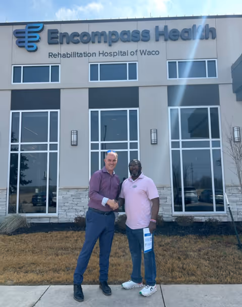 Two men shake hands in front of Encompass Health Rehabilitation Hospital of Waco.