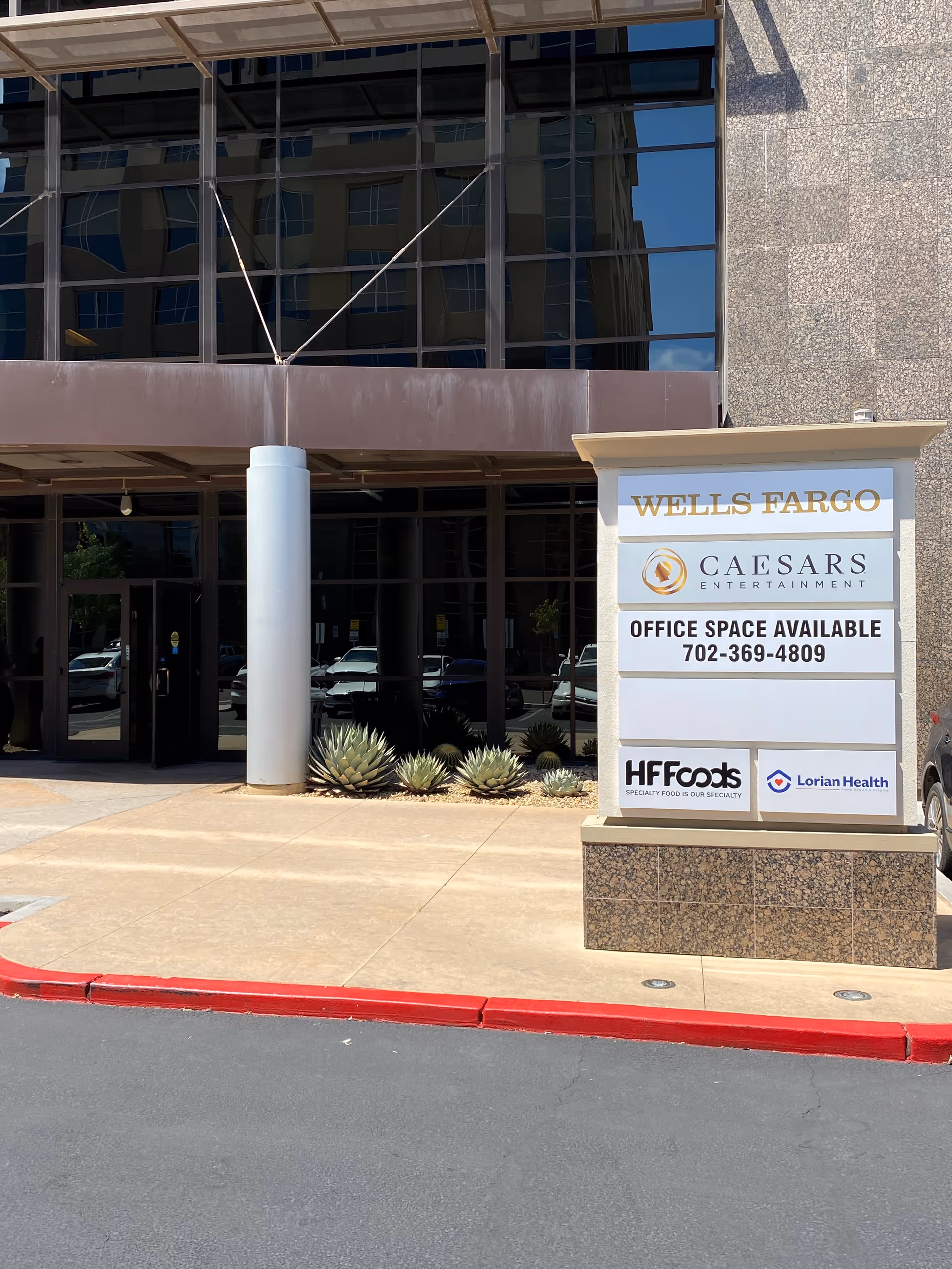 Exterior building entrance with a tall signboard displaying Wells Fargo, Caesars, HF Foods, and Lorian Health.