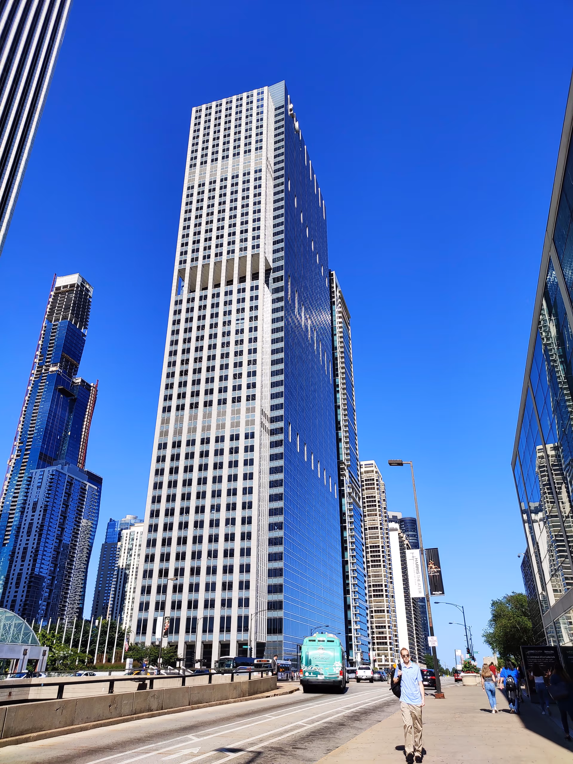 Tall modern skyscraper on a city street under a bright blue sky.