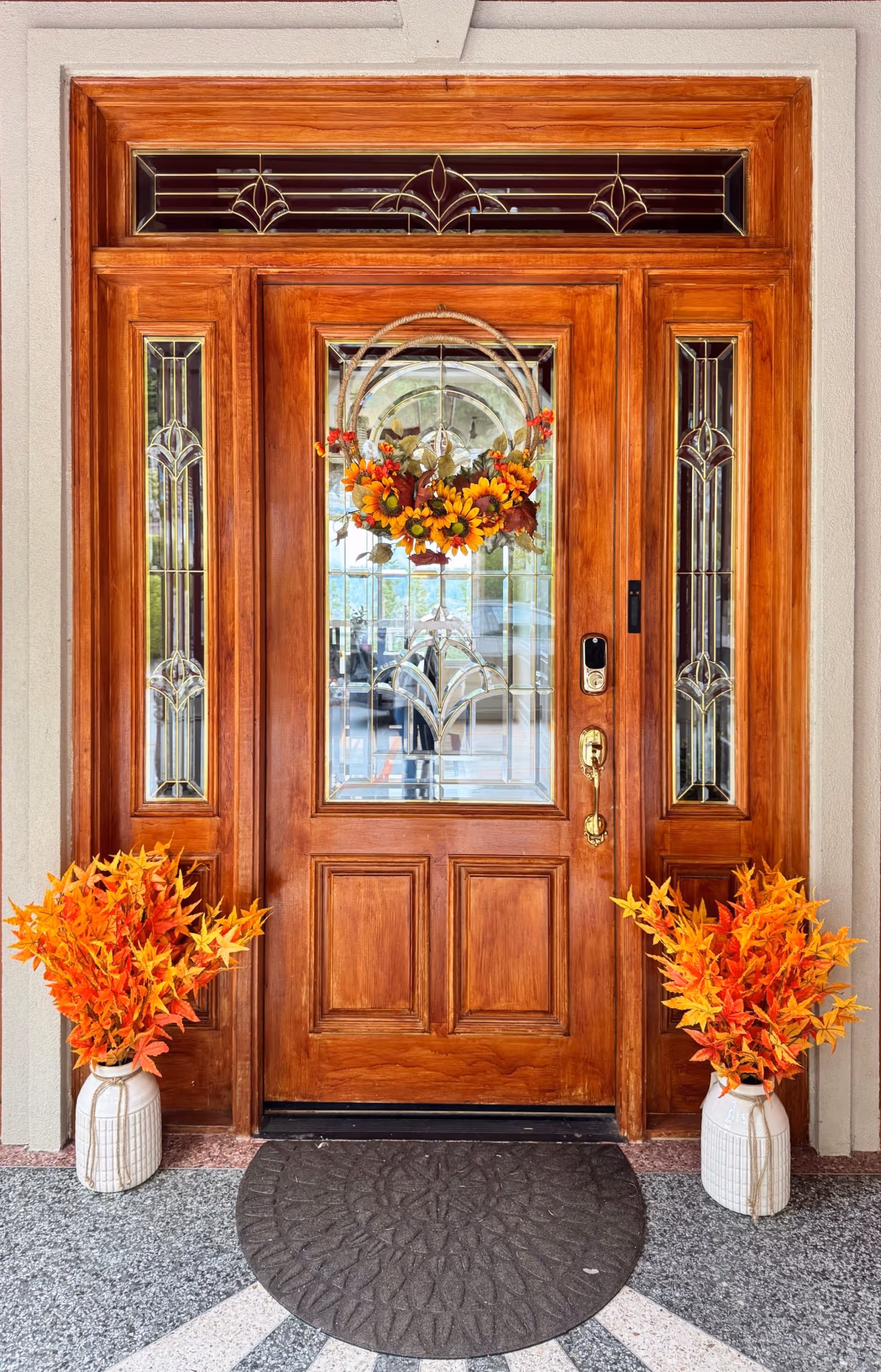 Wooden front door with fall wreath and bright orange seasonal arrangements on both sides.
