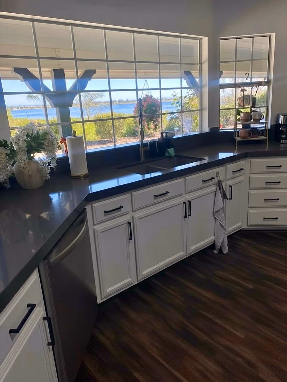 Bright kitchen with white cabinets, dark countertops, and a water view through large windows.