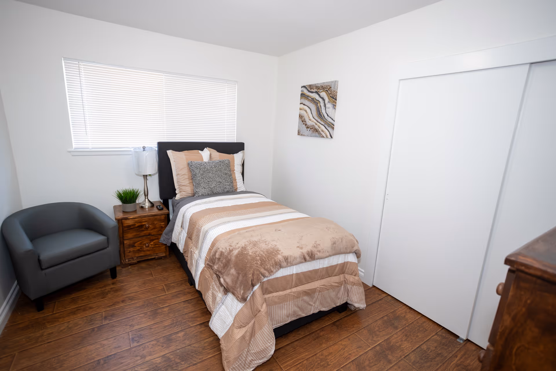 Small bedroom with single bed, nightstand, lamp, chair, and closet doors.