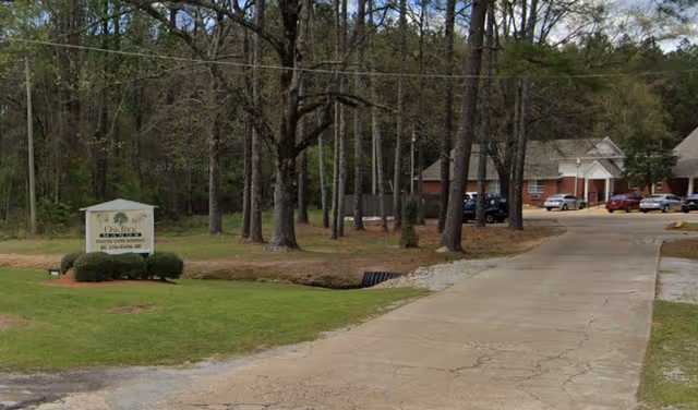Tree-lined driveway leads to Oak Tree Manor Assisted Living exterior with a brick building.