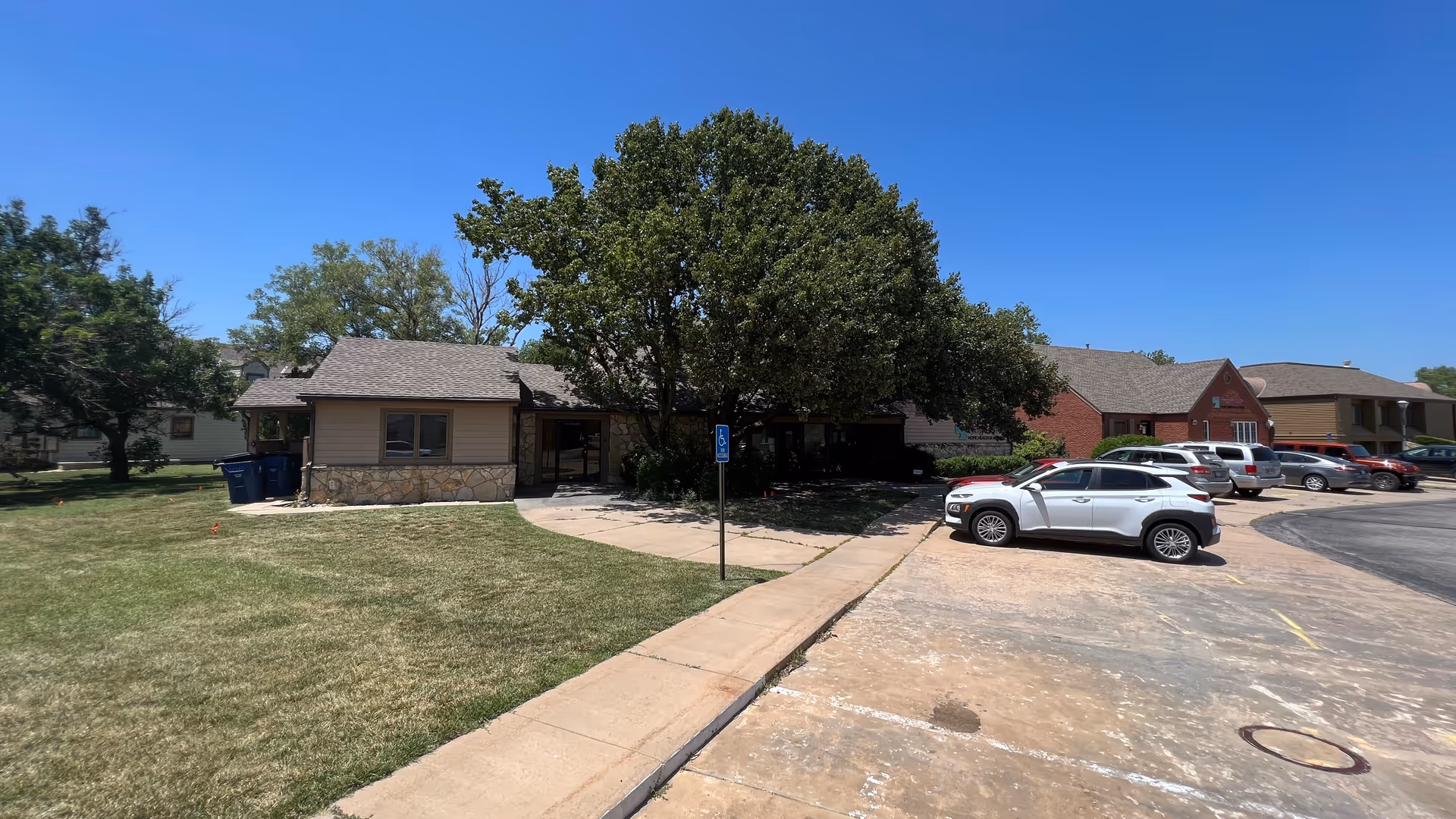Exterior view of a single-story senior facility with trees, sidewalk, and parked cars.